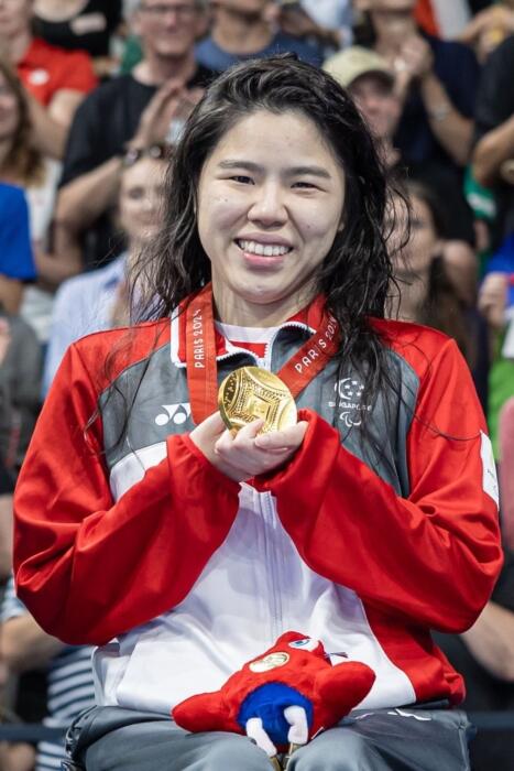 Yip Pin Xiu holding her Paris Paralympics Games gold medal in her hands, smiling and facing the camera. 